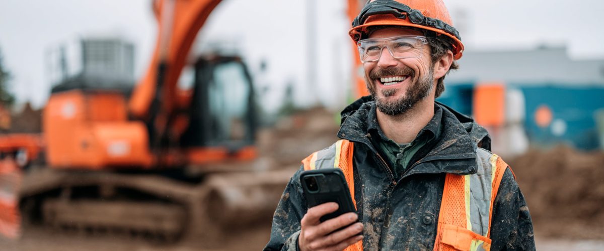 Cheerful construction worker using phone near excavator.