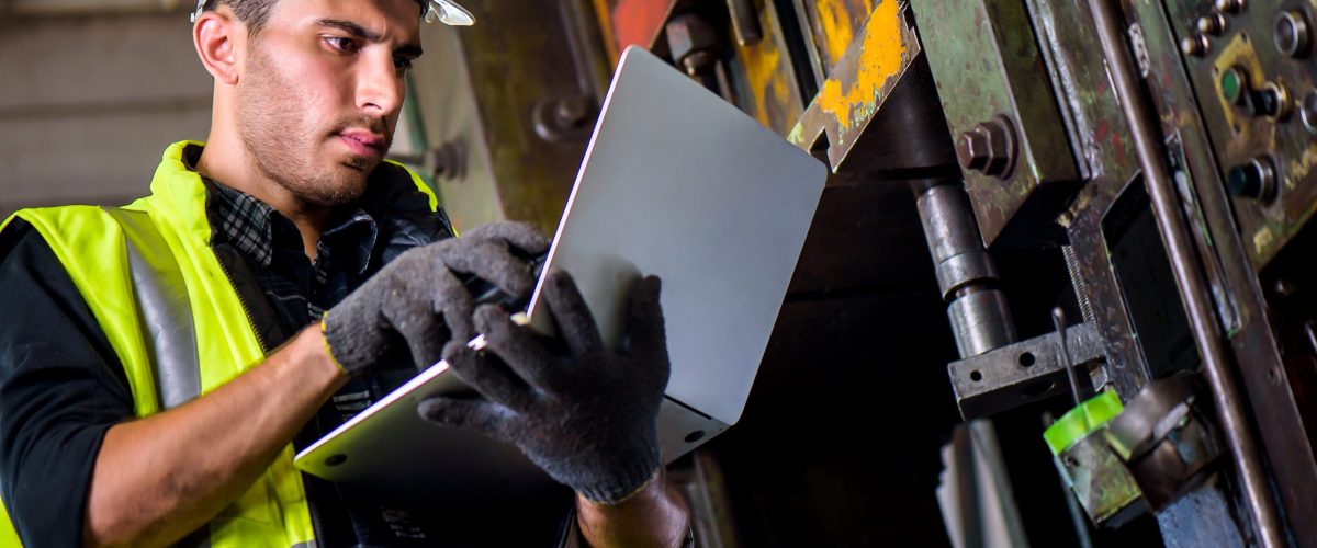 Caucasian engineer mechanic man checking for maintenance pressing metal machine by laptop at factory, worker at industrial concept